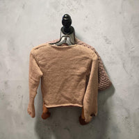 Camel boat-neck knit sweater laid flat, back view, on a pale concrete floor.