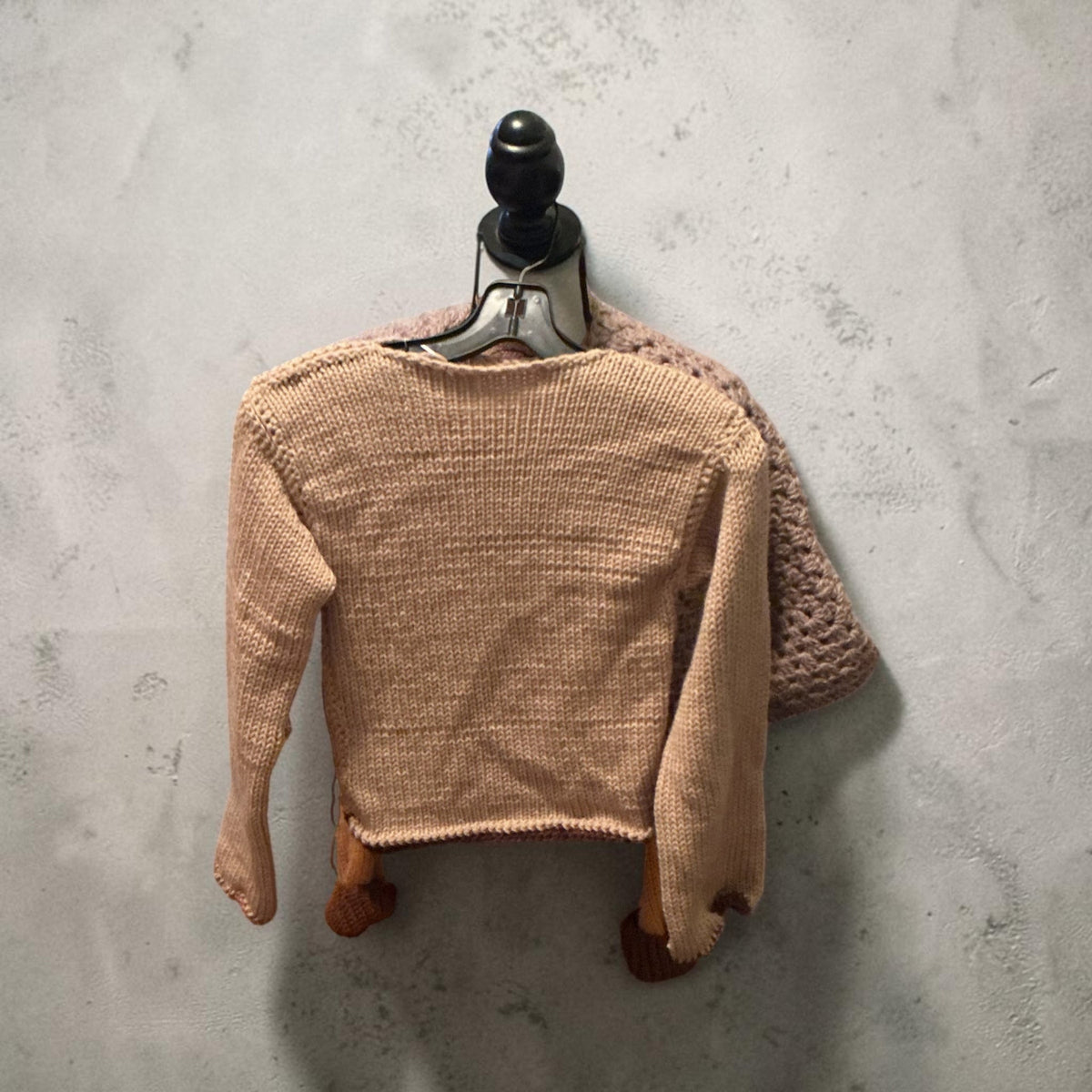 Camel boat-neck knit sweater laid flat, back view, on a pale concrete floor.